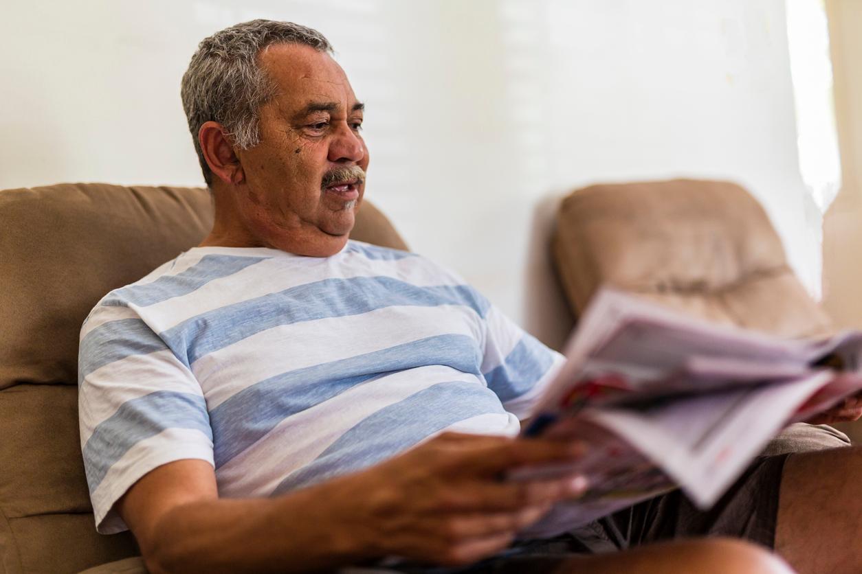 An older man reading a printed booklet in his armchair at home