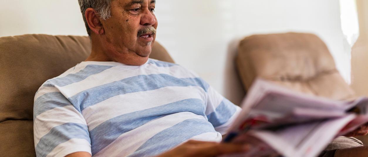 An older man reading a printed booklet in his armchair at home