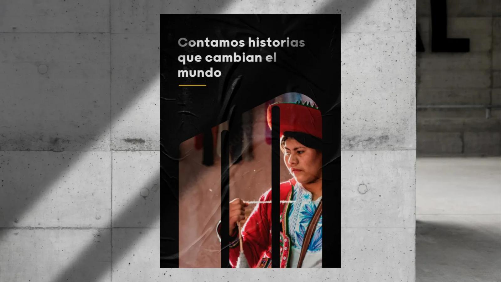 Poster urbano en pared de concreto con fondo negro frase Contamos historias que cambian el mundo y fotografía de mujer tejiendo con vestimenta tradicional andina enmascarada dentro del logotipo de tres barras