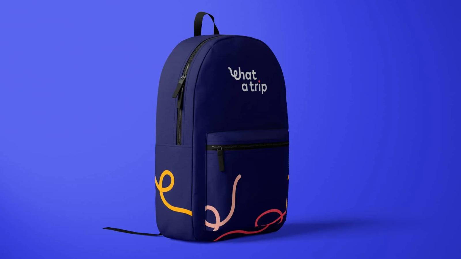 Mochila de color azul oscuro sobre fondo azul vibrante, decorada con el logotipo de 'What a Trip' en blanco en la parte superior y trazos ondulados amarillos y rojizos en el bolsillo frontal