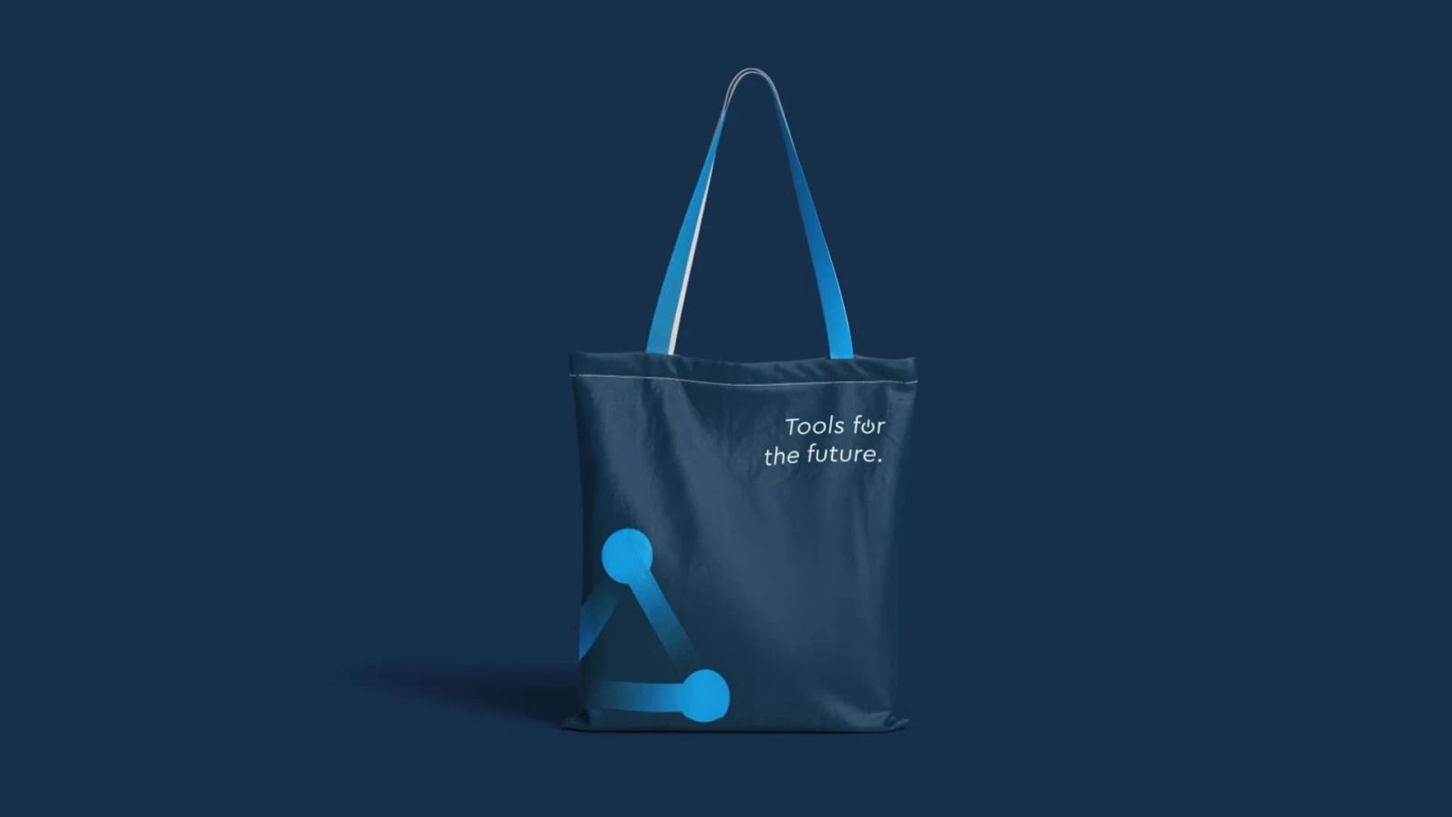 Mockup de bolsa de tela (tote bag) corporativa de Adiss en azul oscuro, con el diseño del isotipo de nodos en la esquina y el eslogan 'Tools for the future' en blanco