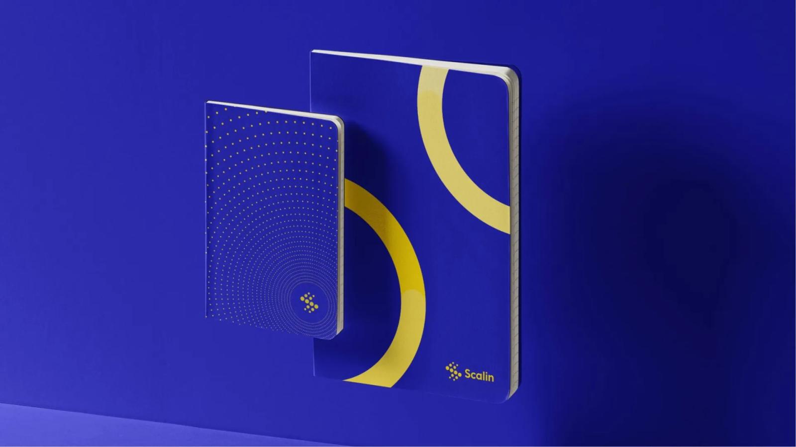 Dos cuadernos corporativos Scalin flotando en el aire con diseños de ondas lineales y degradado en tonos azules y amarillos