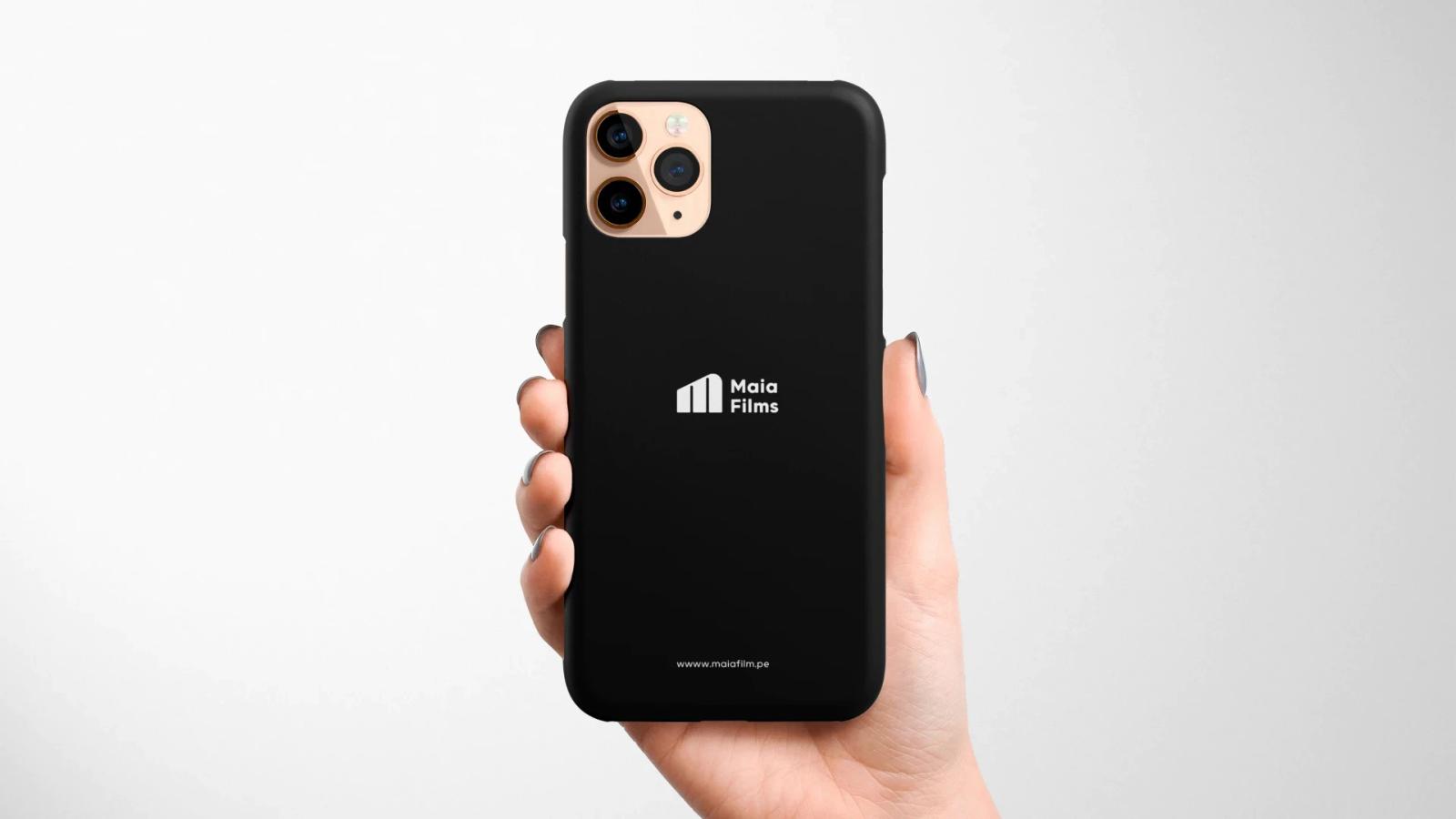 Mockup de funda negra para smartphone sostenida por una mano mostrando el logotipo blanco de Maia Films en la parte posterior sobre un fondo claro y limpio