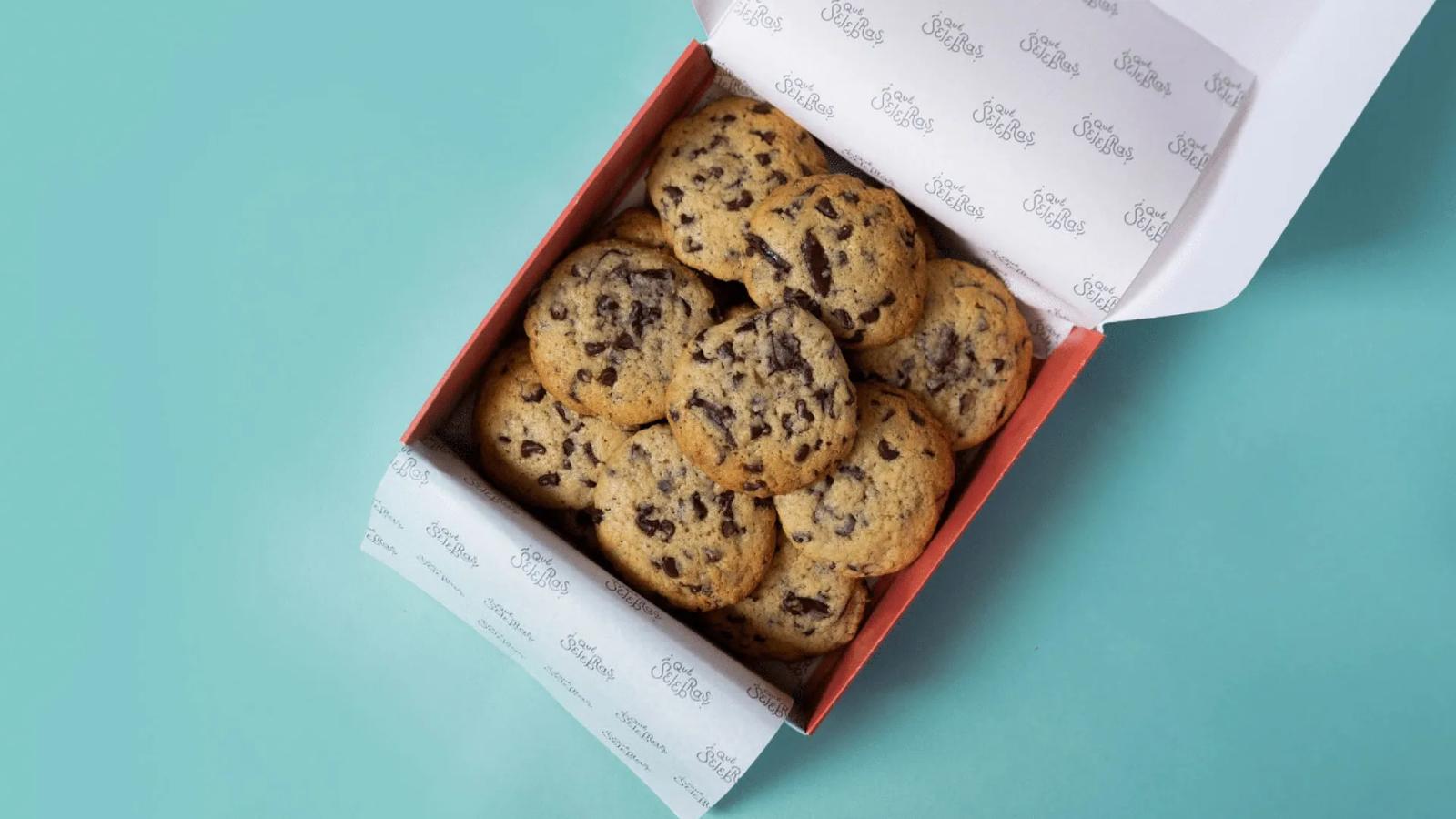 Caja abierta con galletas con chispas de chocolate presentadas sobre fondo de color pastel