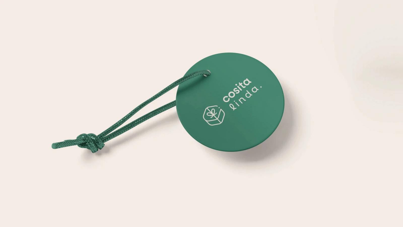 Etiqueta redonda de color verde oscuro con un cordón anudado, presentando el logotipo y el ícono de regalo de Cosita Linda, en color crema sobre un fondo neutro