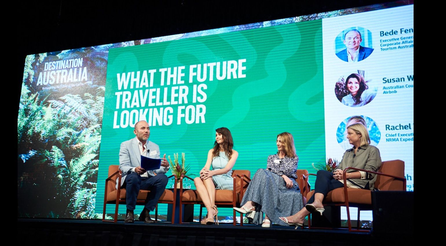A group of speakers on stage in front of a large screen