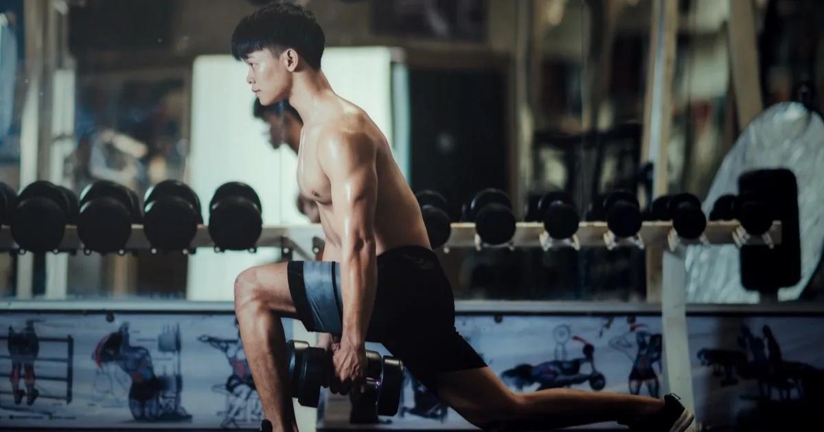 นักกีฬาไทยชายวัย 35 ยืนพักหลังวิ่งเทรลยามเช้าในกรุงเทพฯ มือเท้าสะเอวมองไปไกลๆ ด้วยสีหน้าครุ่นคิด แสงธรรมชาติสีทองอบอุ่น
