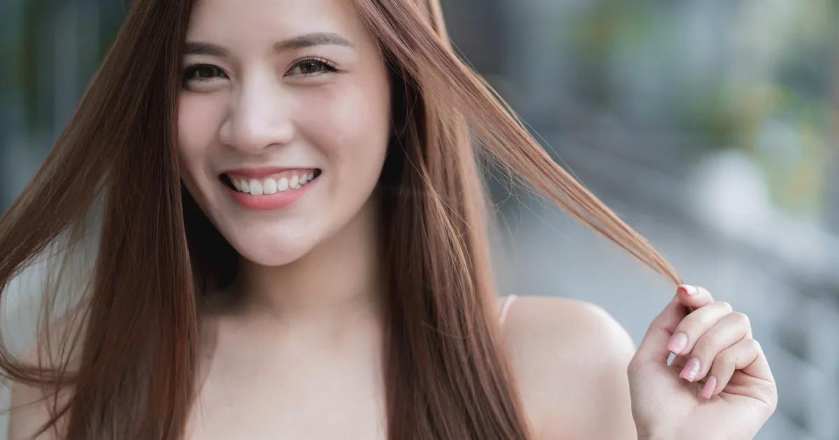 หญิงเอเชียยิ้มมั่นใจ ถือปลายผมยาวสลวยเป็นประกาย สื่อถึงผลลัพธ์เส้นผมแข็งแรงหลังจากดูแลฮอร์โมนให้สมดุล