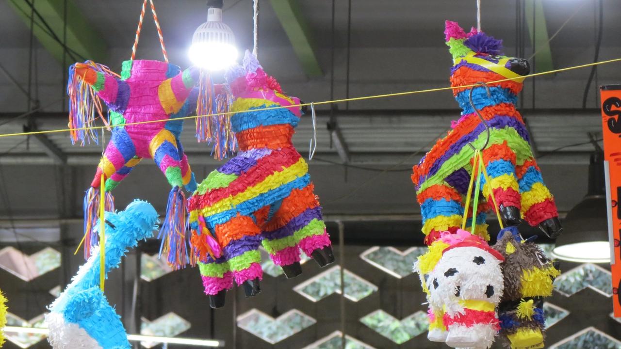Interior del Mercado de San Juan, en la Ciudad de México, con piñatas colgadas sobre los puestos.