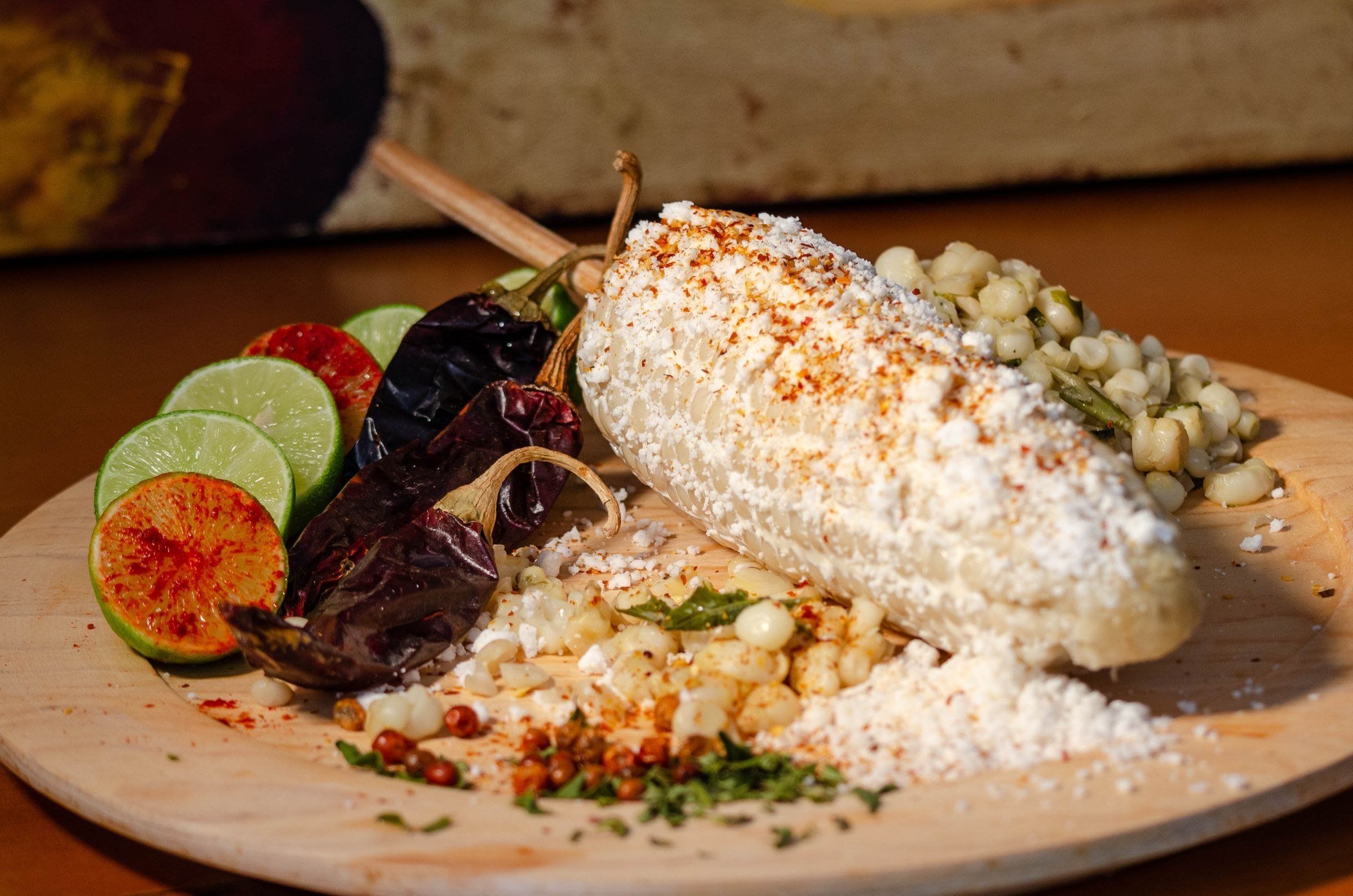 Elote con queso y chile junto a esquites y limones en un plato de madera (imagen de archivo).