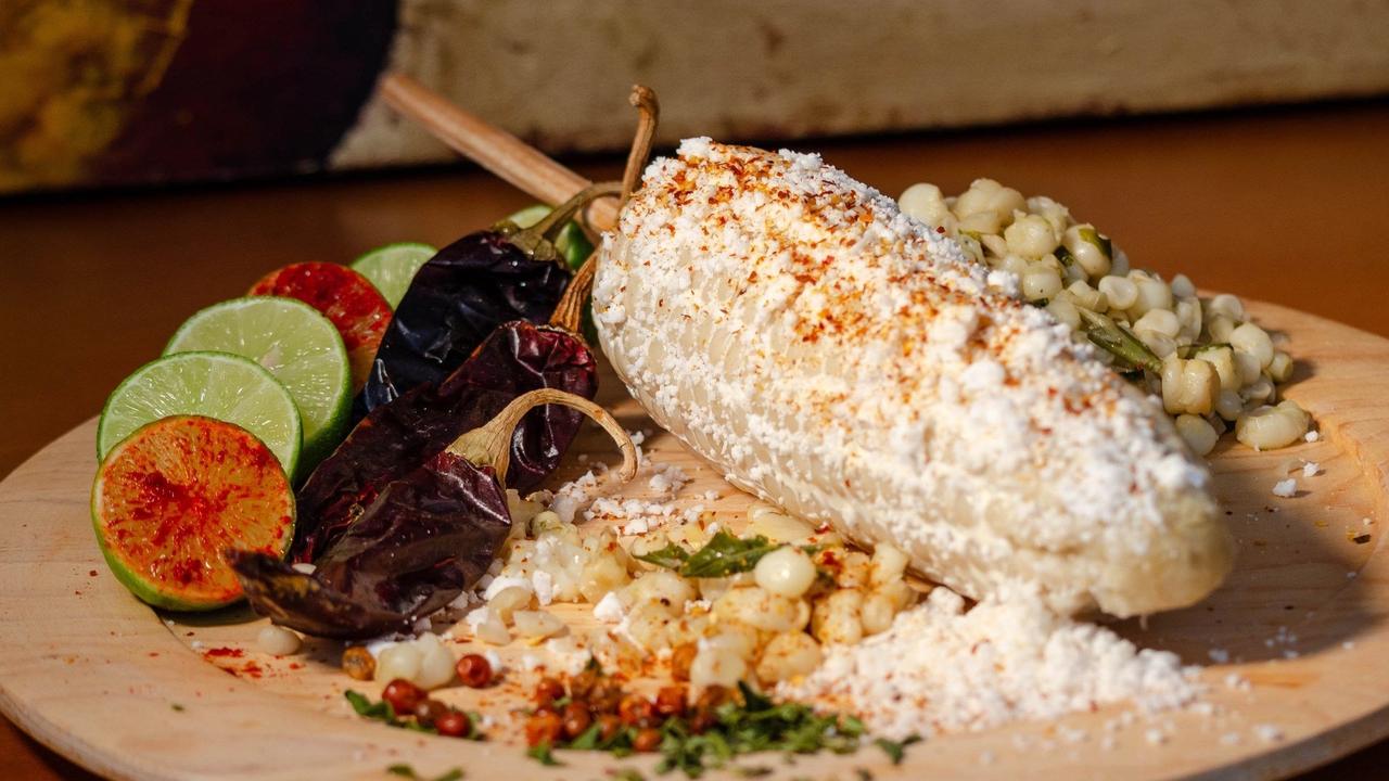 Elote con queso y chile junto a esquites y limones en un plato de madera (imagen de archivo).