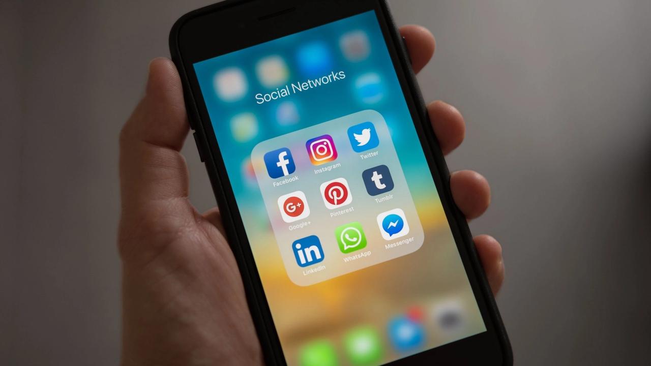 Persona sostiene un teléfono con una carpeta de redes sociales en la pantalla (imagen de archivo).