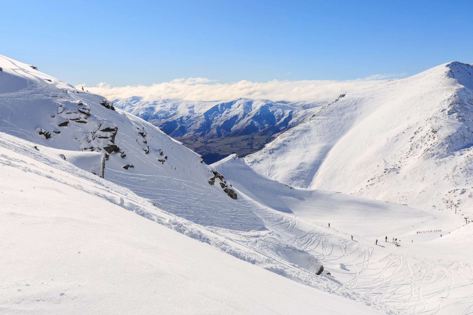 Snow-covered slopes at Coronet Peak with a clear view of the valley and distant mountains under a bright blue sky