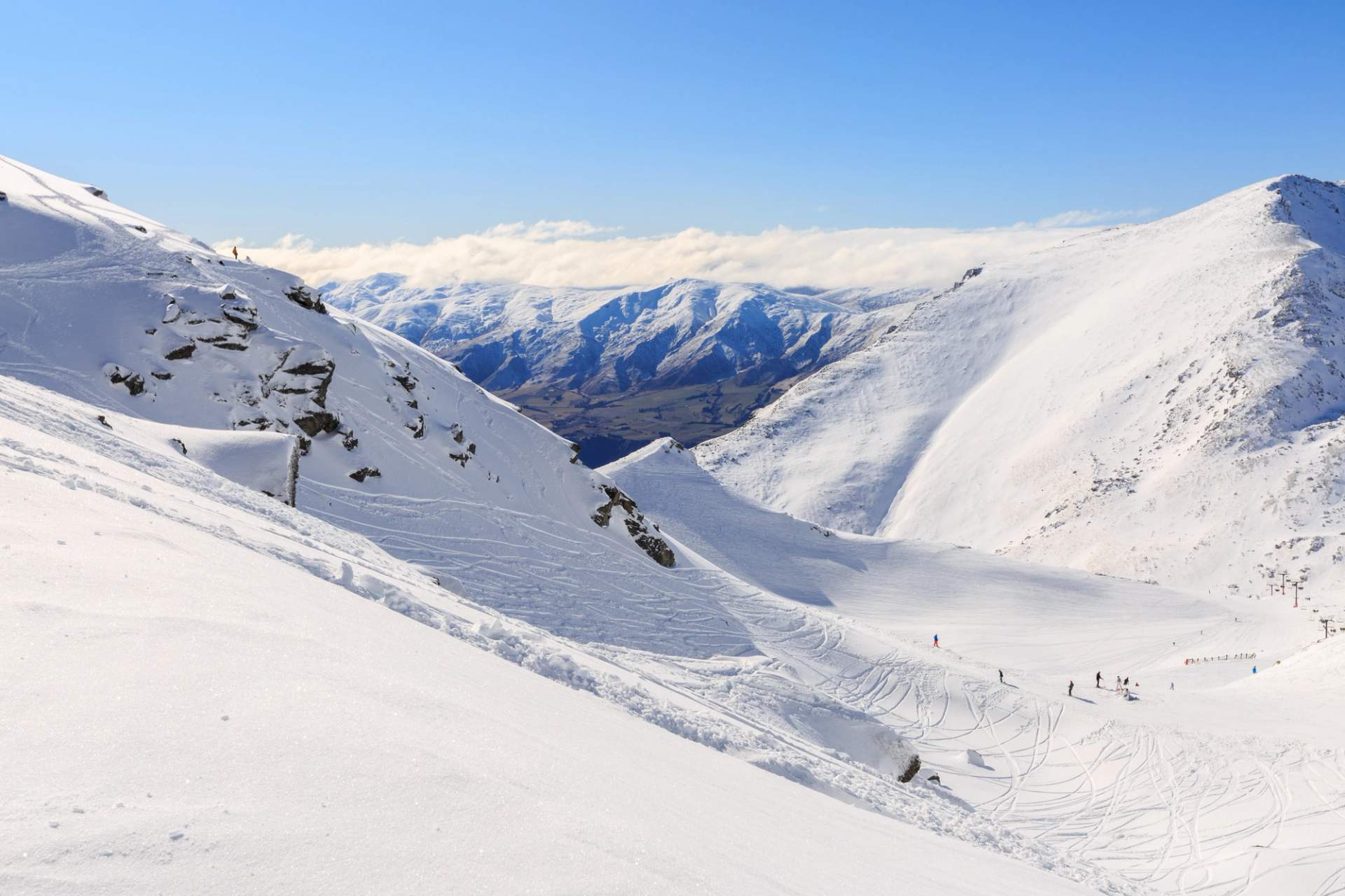 Snow-covered slopes at Coronet Peak with a clear view of the valley and distant mountains under a bright blue sky