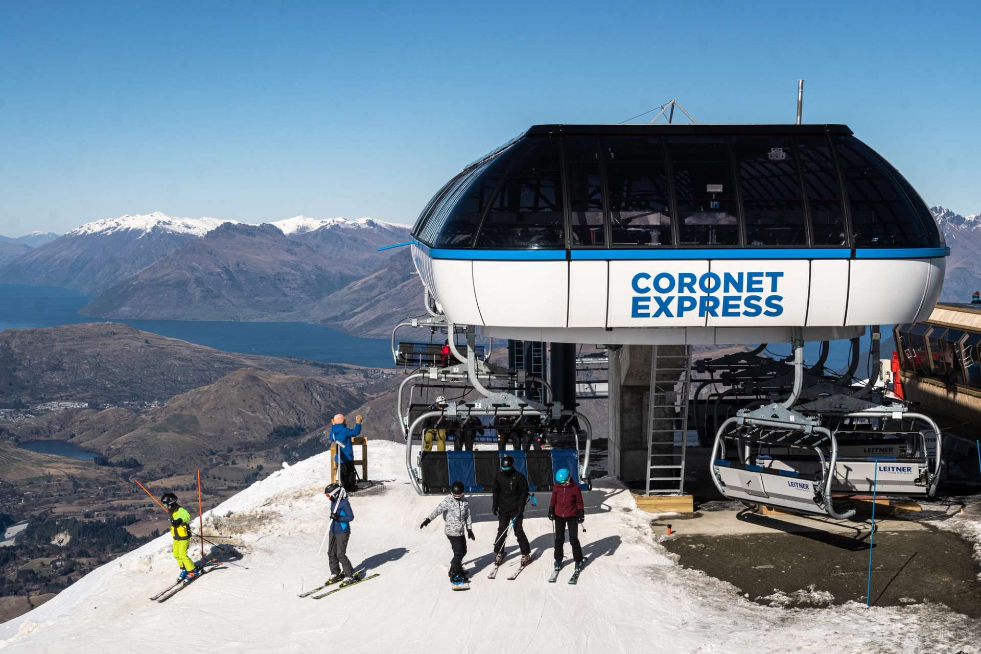 View of the Coronet Express chairlift at Coronet Peak with snow-covered mountains in the background and skiers at the base.