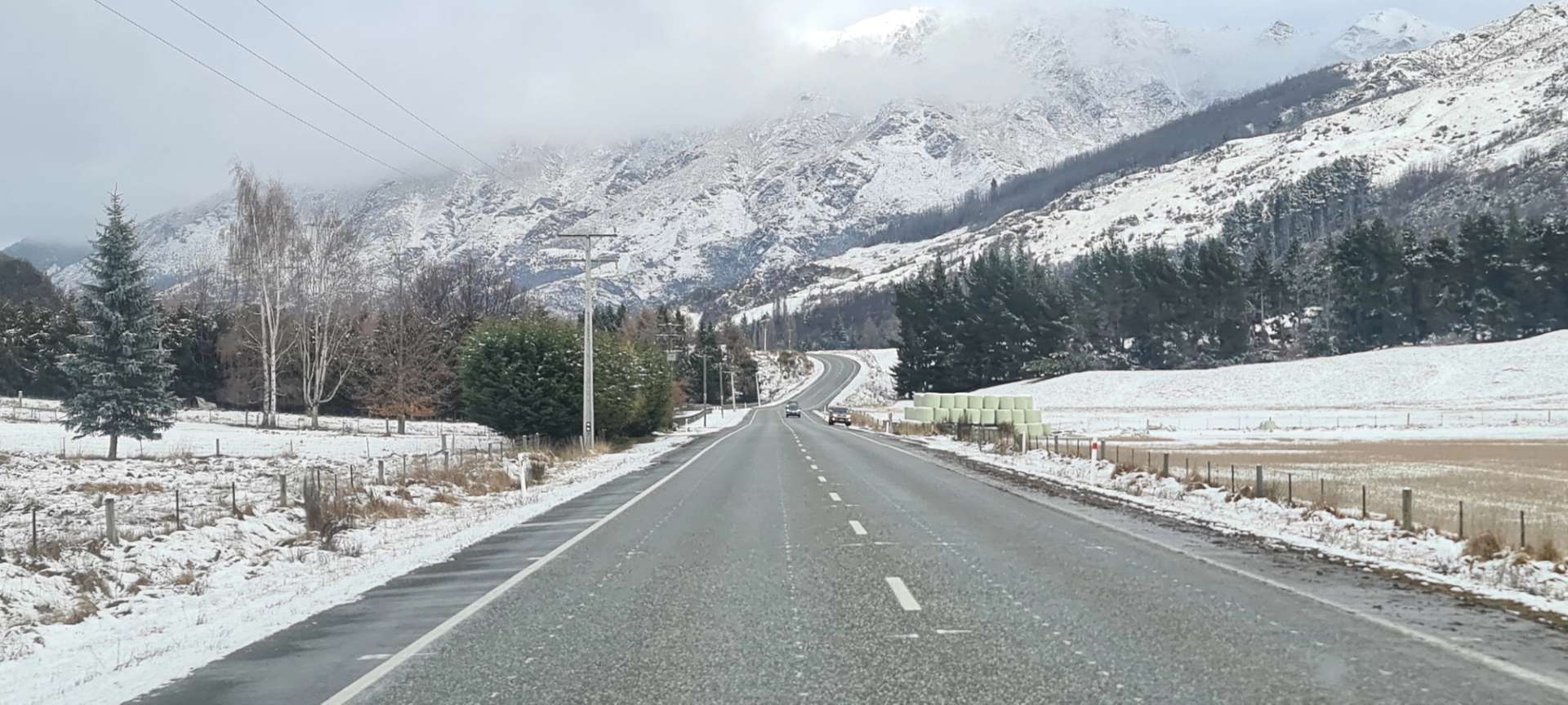 Snow-lined road winding toward The Remarkables with alpine trees and misty mountain peaks in the distance