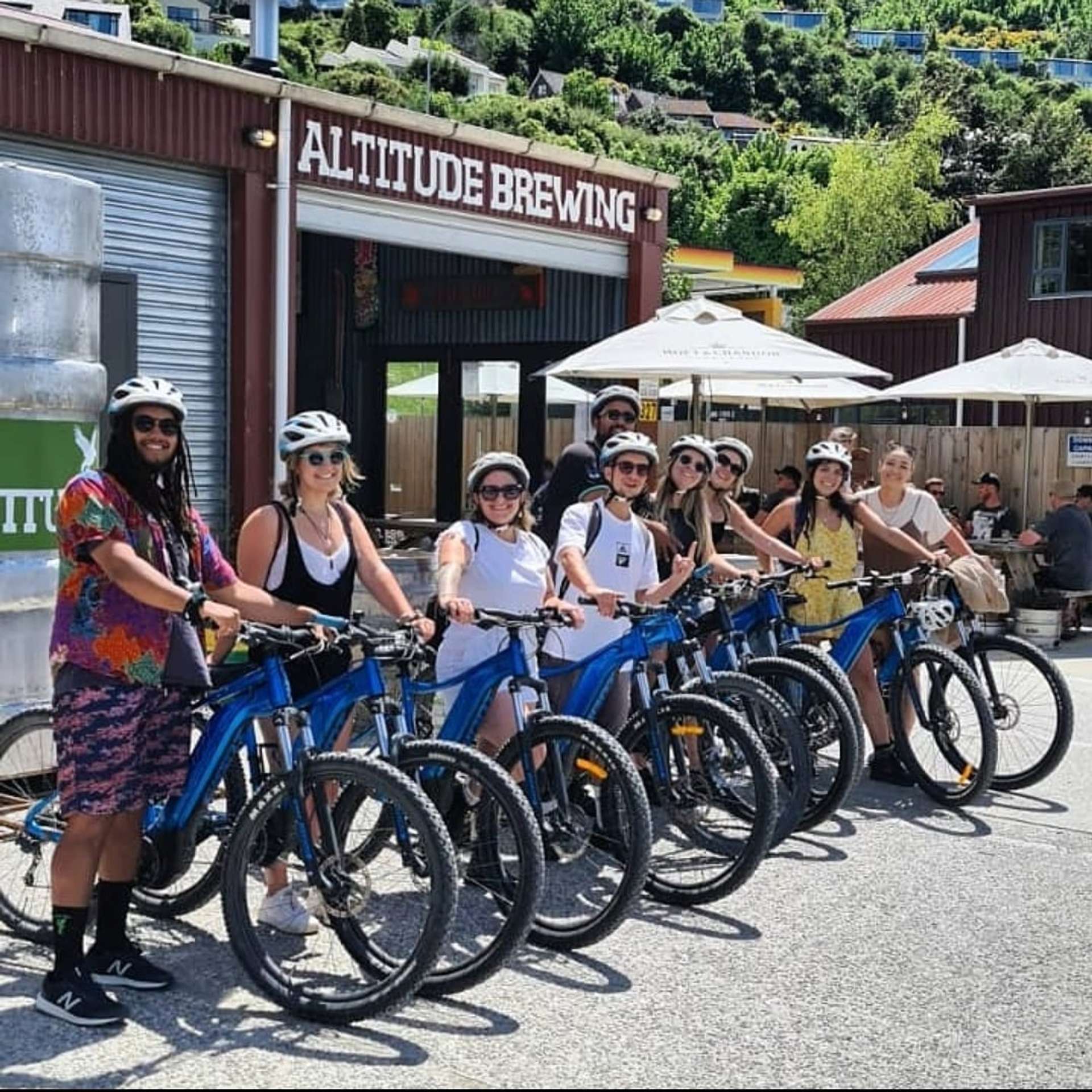 Group of cyclists outside Altitude Brewery after completing the Shotover River Trail, enjoying sunshine and craft beers