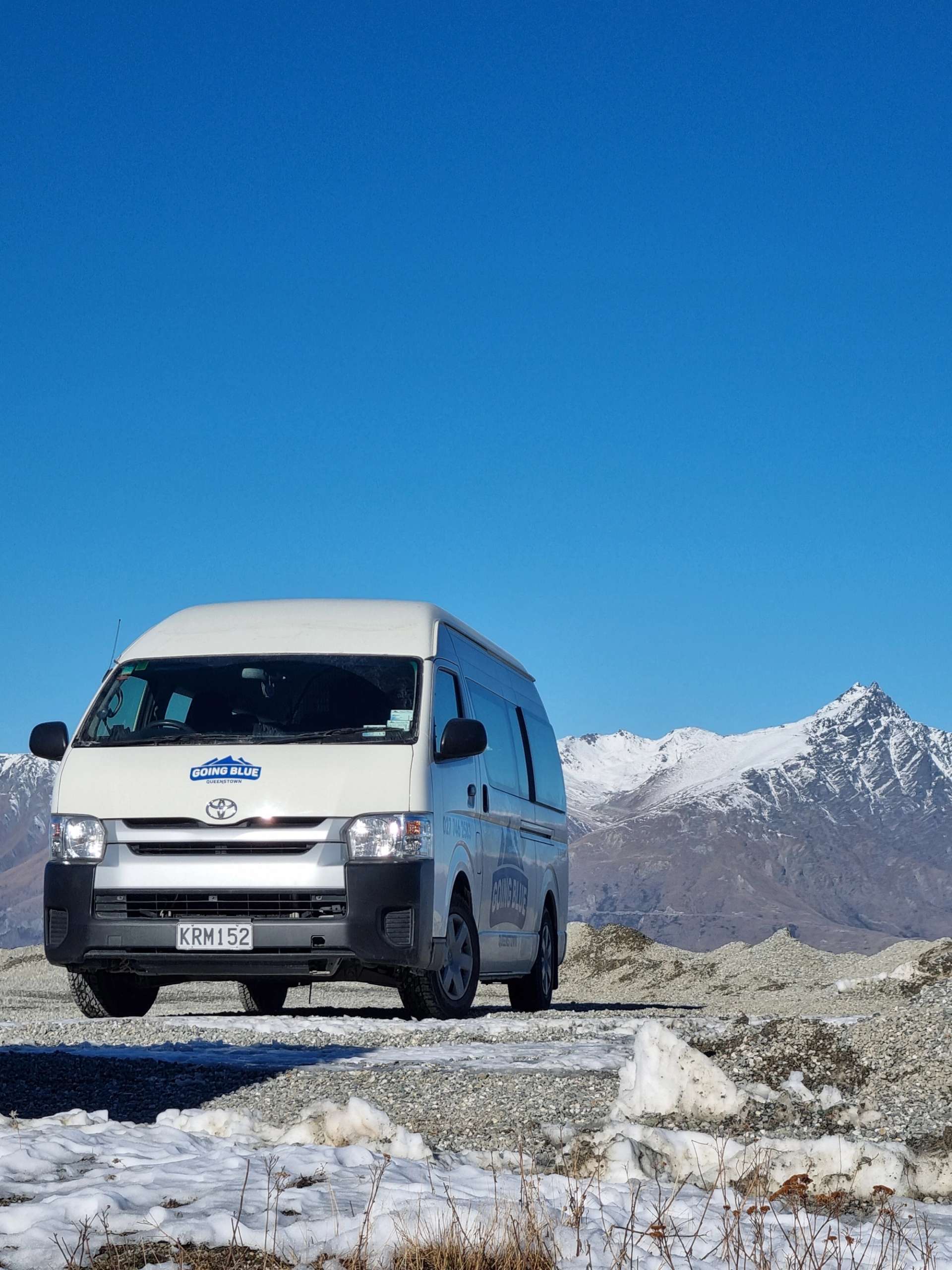 Going Blue ski transport van parked on snowy terrain with the Remarkables mountain range in the background under clear blue skies