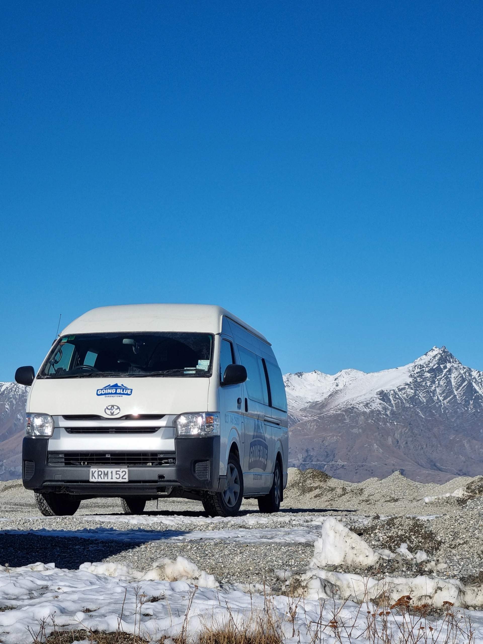 Going Blue ski transport van parked on snowy terrain with the Remarkables mountain range in the background under clear blue skies