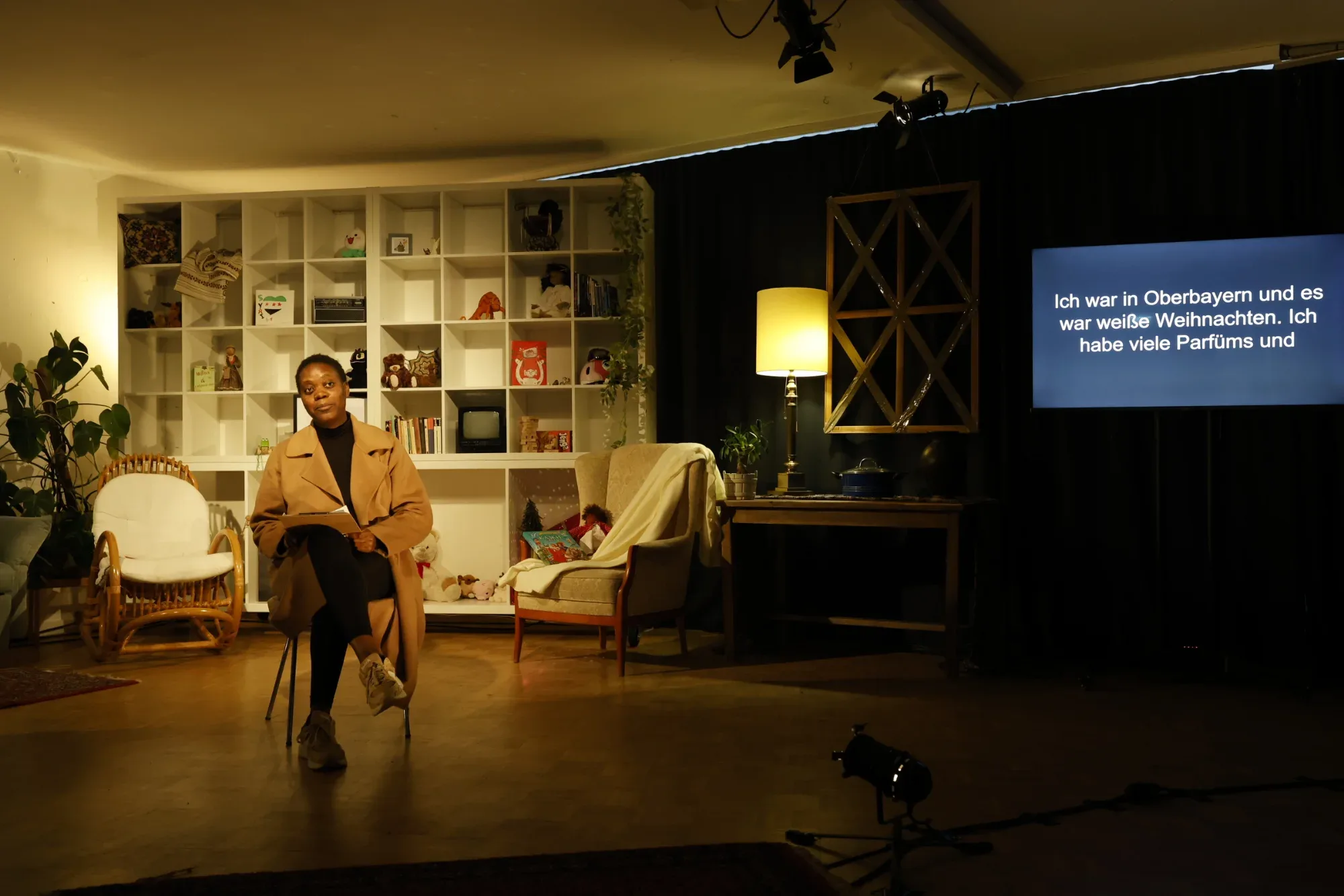 The stage of TAKE ME HOME: a living room, with German subtitles on a screen.