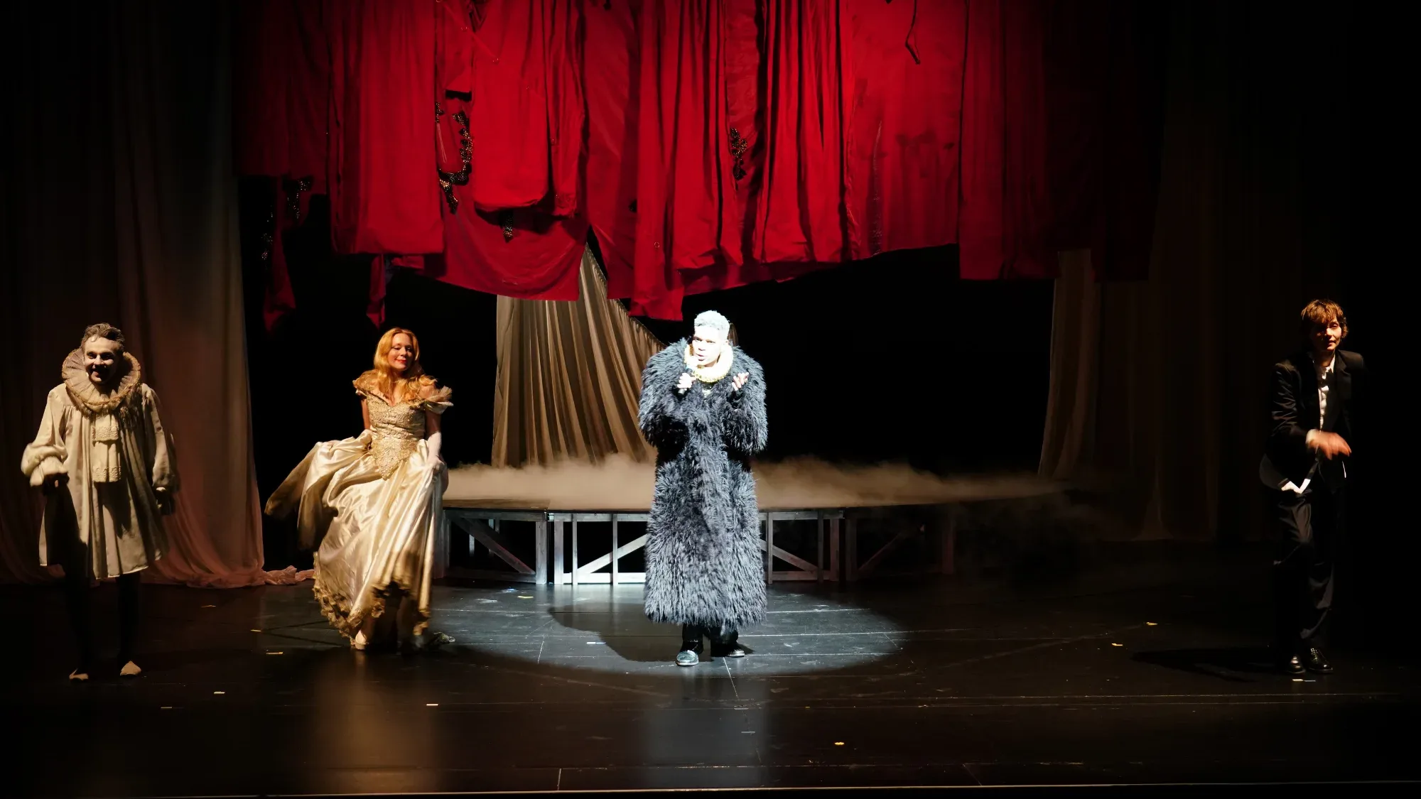 Figures in costume before red curtains.