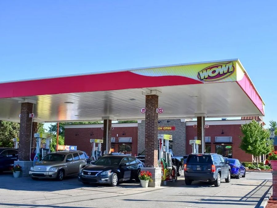 WOW station canopy with a red and yellow wave fascia over cars at the pumps