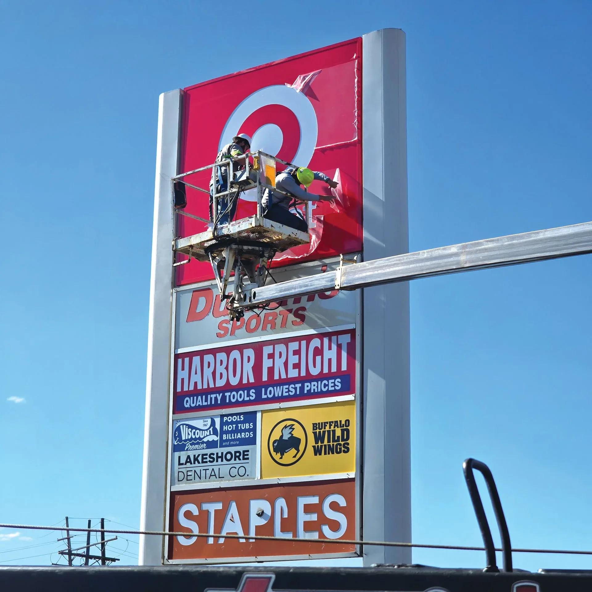 Technician in a bucket truck working on a multi-tenant pylon sign with Target, Harbor Freight and Staples panels