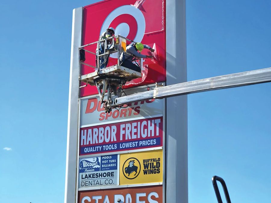 Technician in a bucket truck working on a multi-tenant pylon sign with Target, Harbor Freight and Staples panels