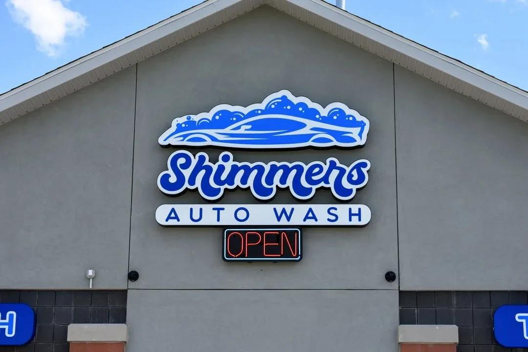 Shimmers Auto Wash logo sign above a lit OPEN sign on a grey wall