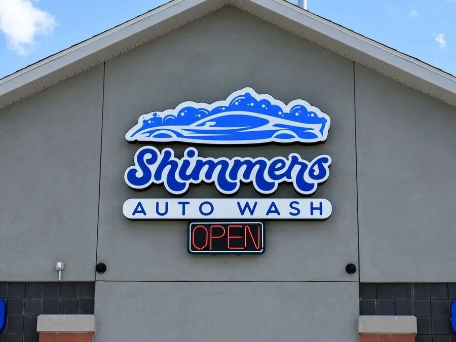 Shimmers Auto Wash logo sign above a lit OPEN sign on a grey wall