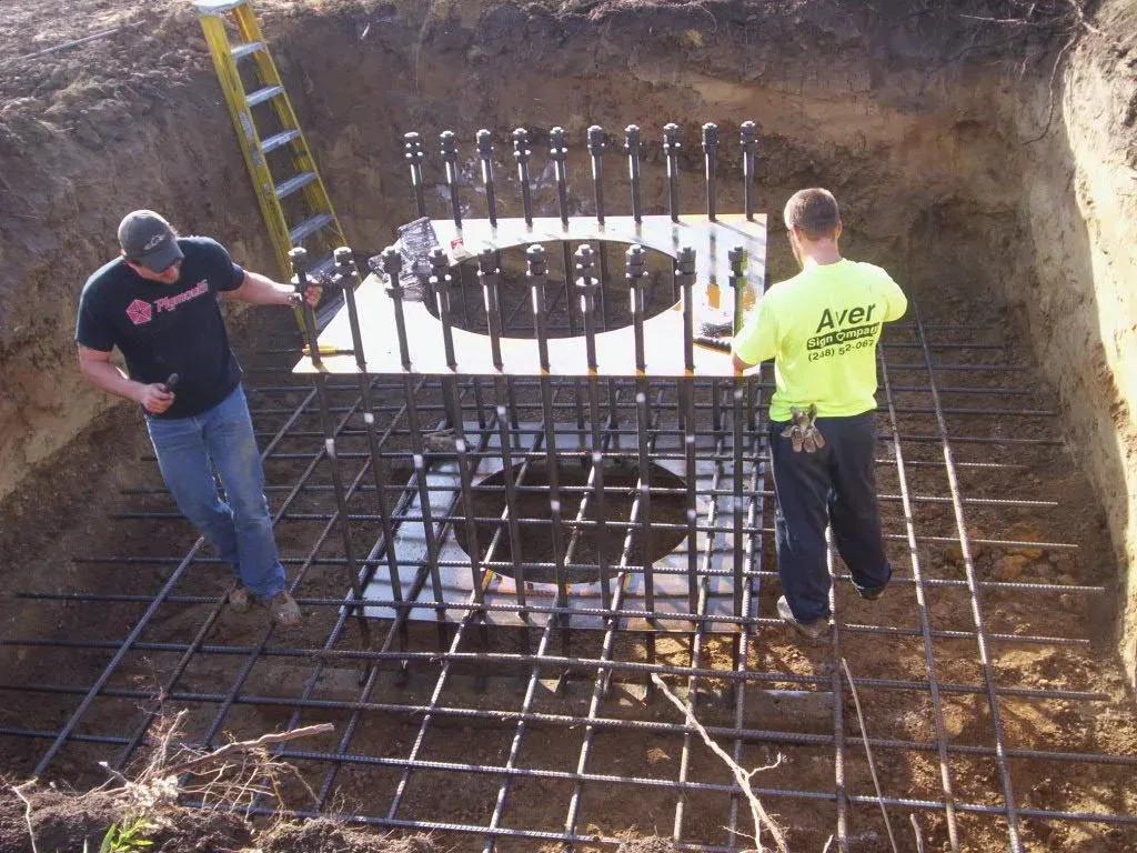 Two installers checking a rebar cage and anchor bolts in a sign footing excavation