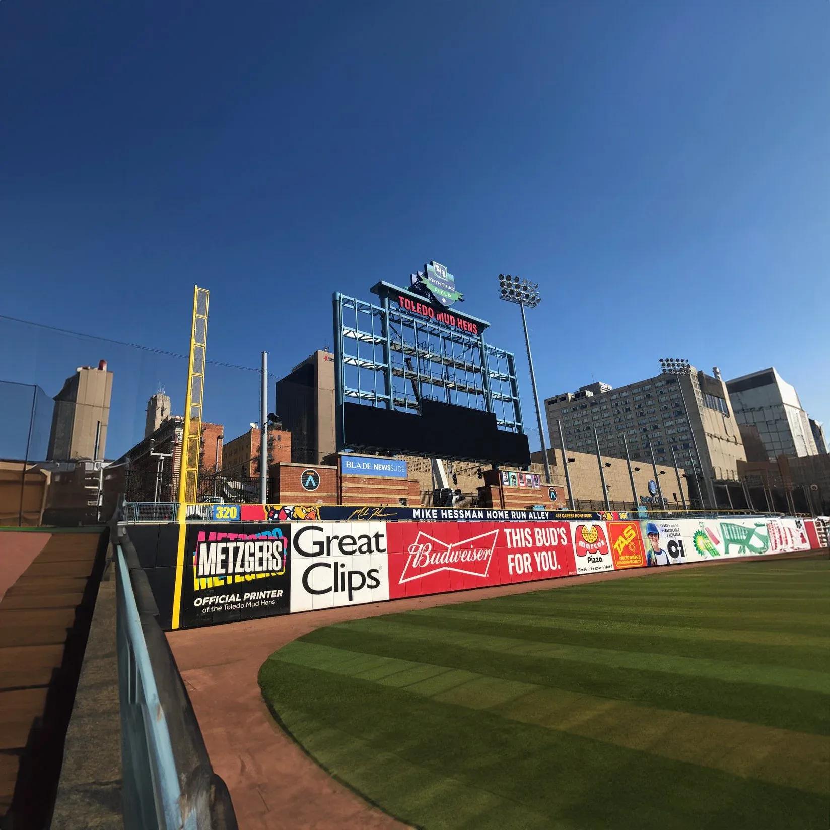 Wide view of a ballpark outfield with the video scoreboard and signs along the outfield wall