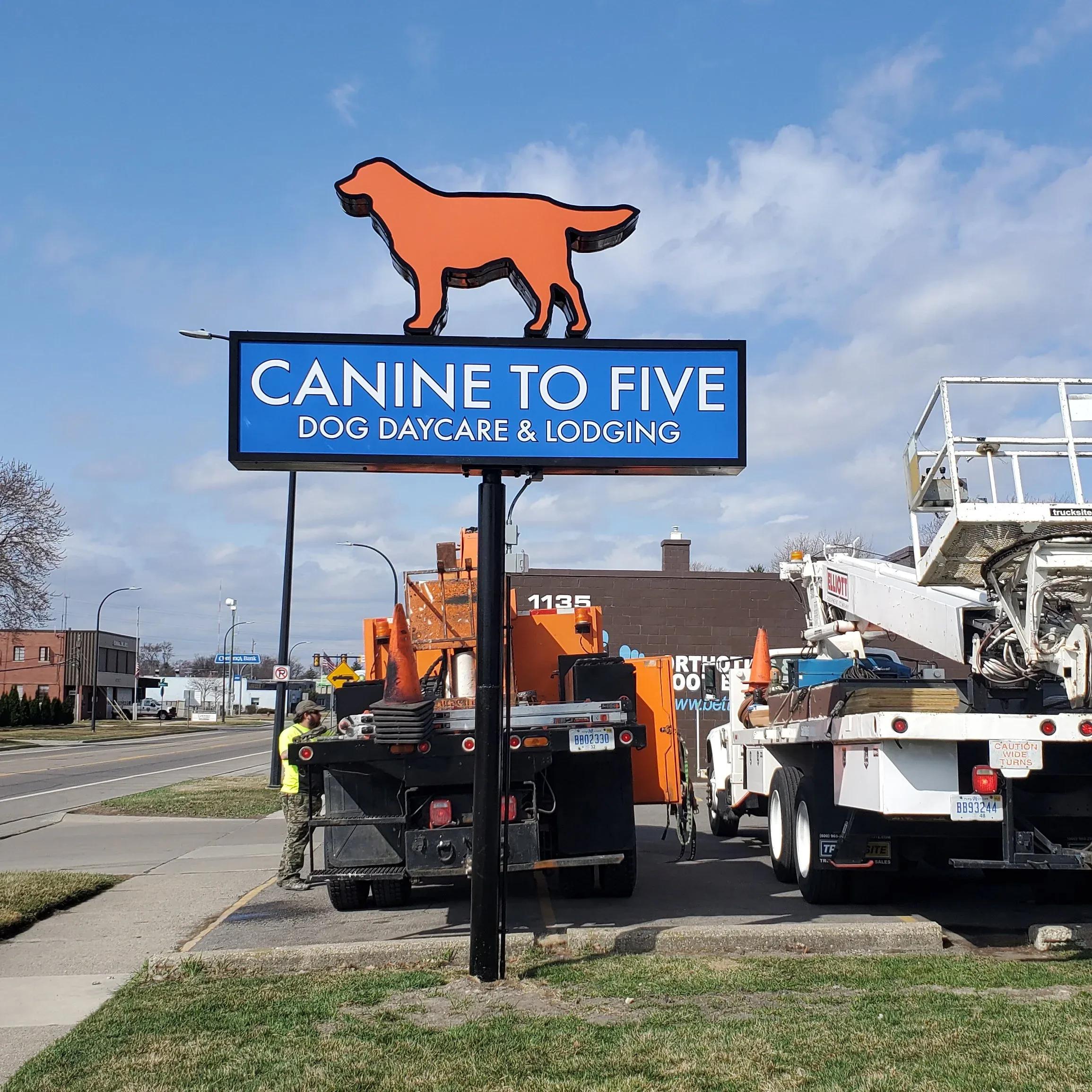 Two crane trucks beside a new Canine to Five pylon sign with a dog-shaped cabinet on top