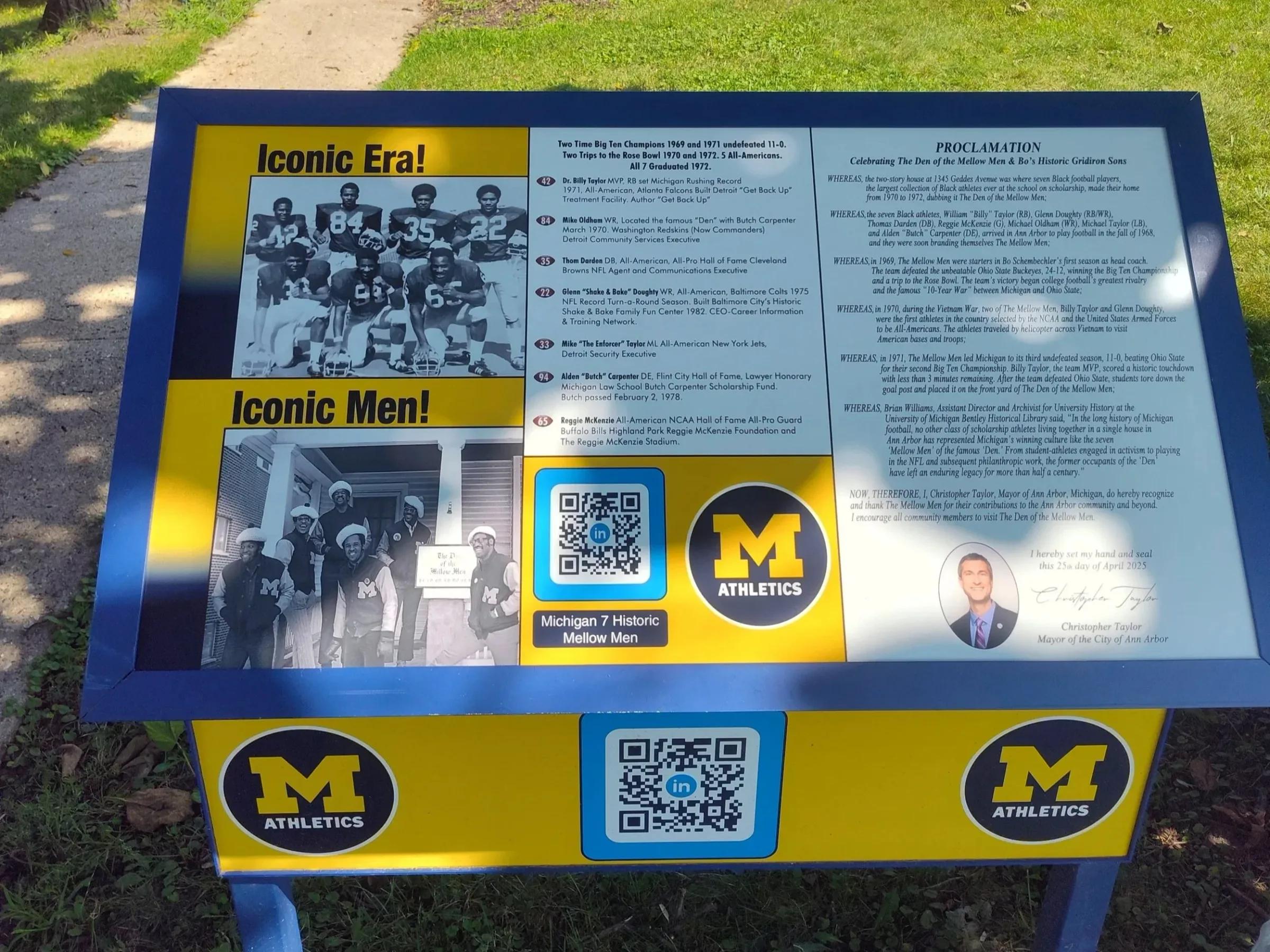 Blue and maize interpretive marker with historic photos, text and QR codes beside a sidewalk