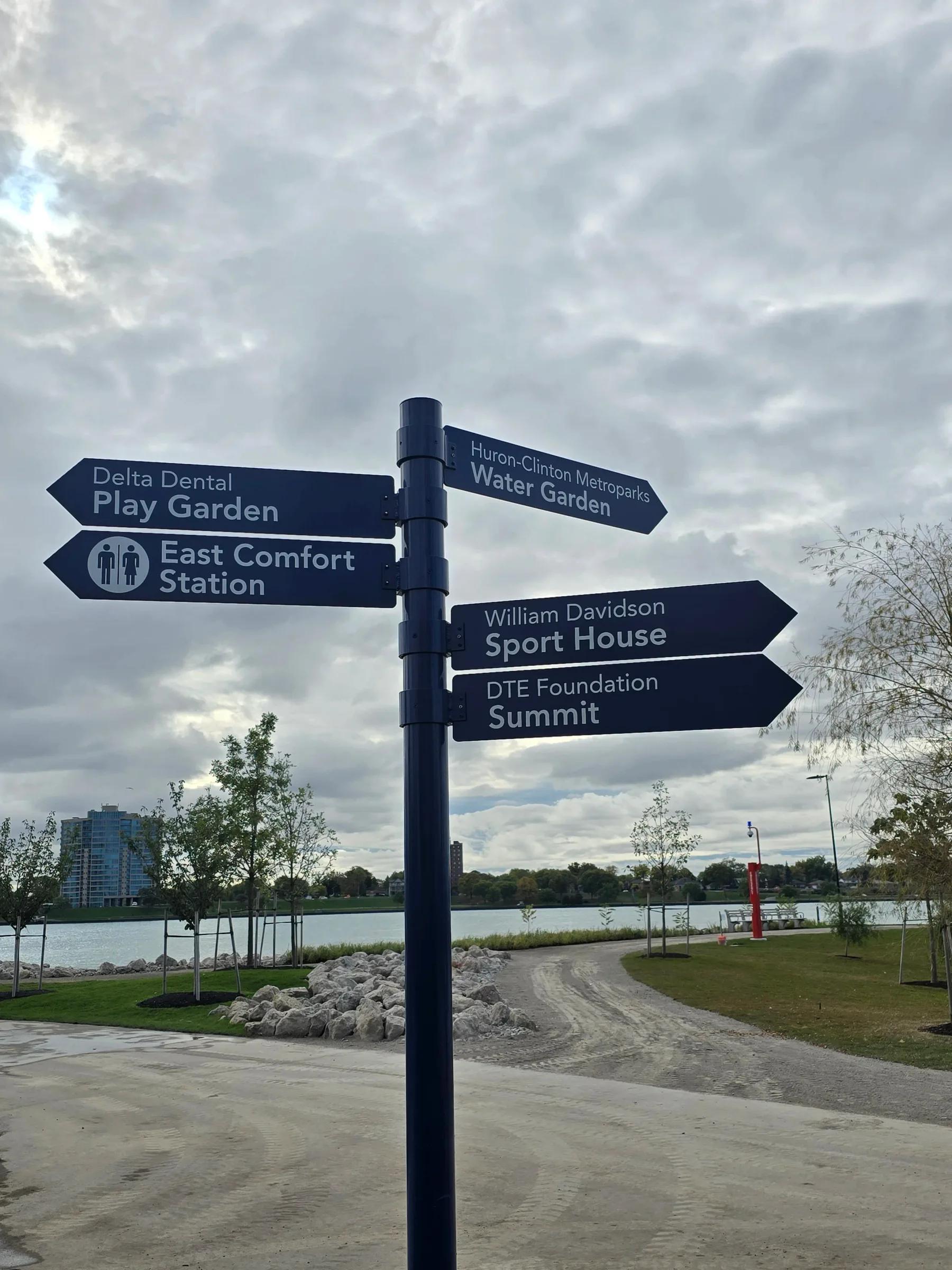 Dark blue wayfinding post with directional arrow signs beside a waterfront path
