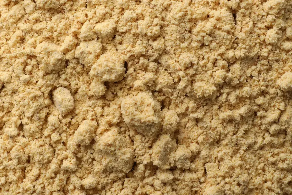 Een close-up van grove gemalen gele mosterd, waarop de korrelige textuur en rijke gele kleur te zien zijn.