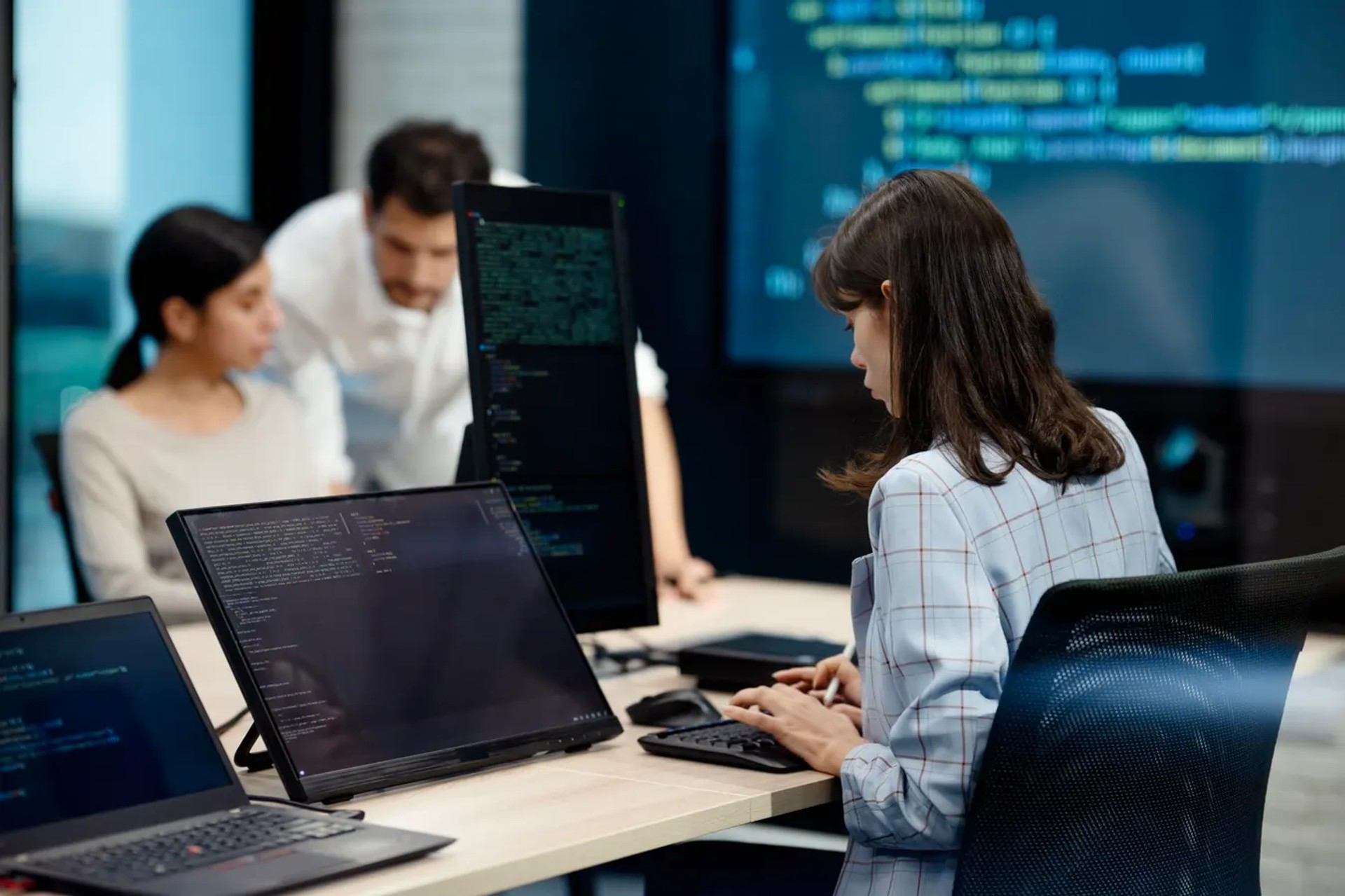 Team of engineers reviewing code on multiple monitors in an office