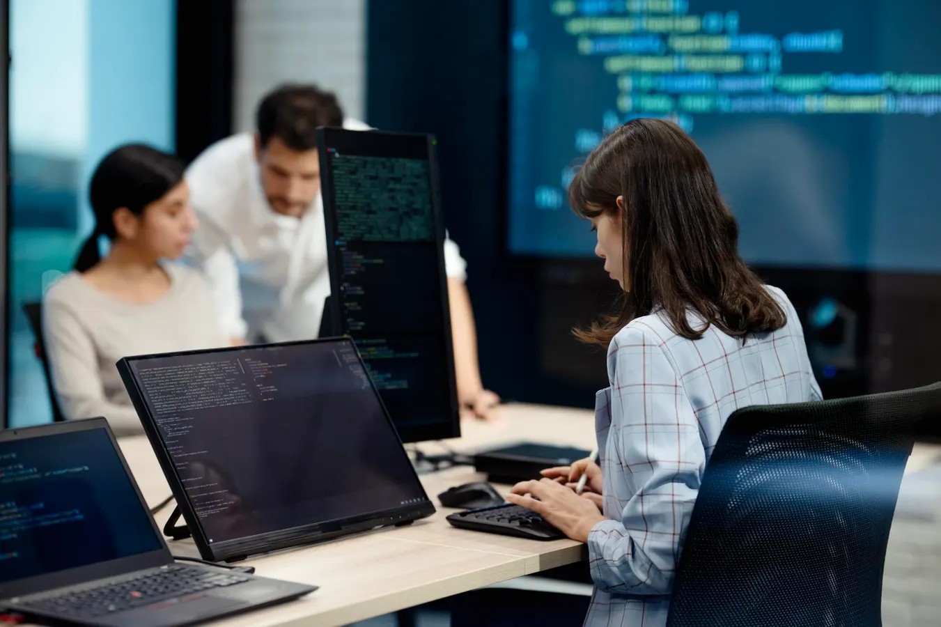 Team of engineers reviewing code on multiple monitors in an office