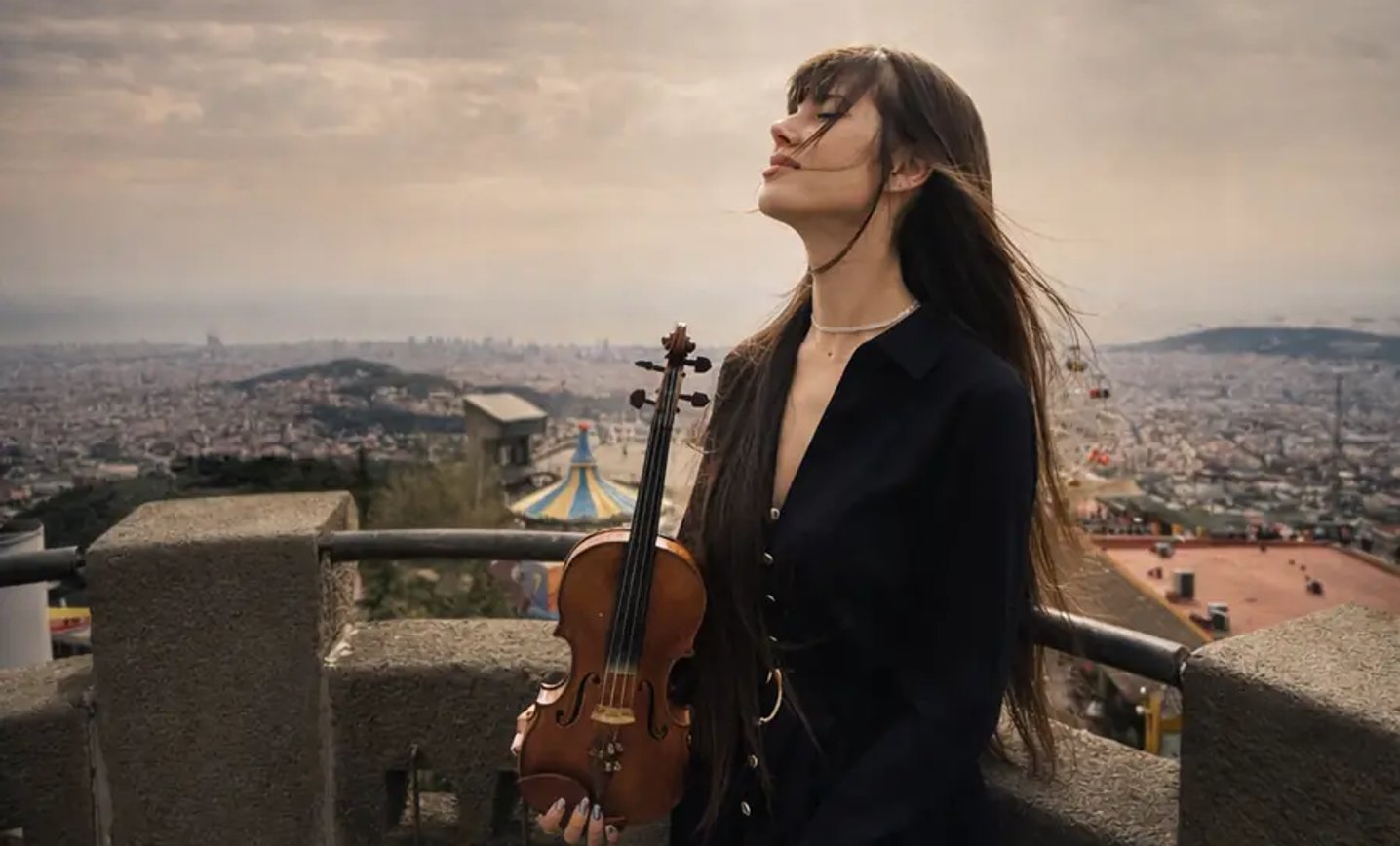 Astrid Torrente con su violín acústico, de espaldas al perfil de Barcelona al atardecer.