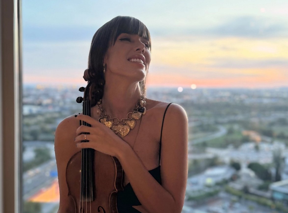 Astrid Torrente con su violín junto a una ventana, al atardecer.