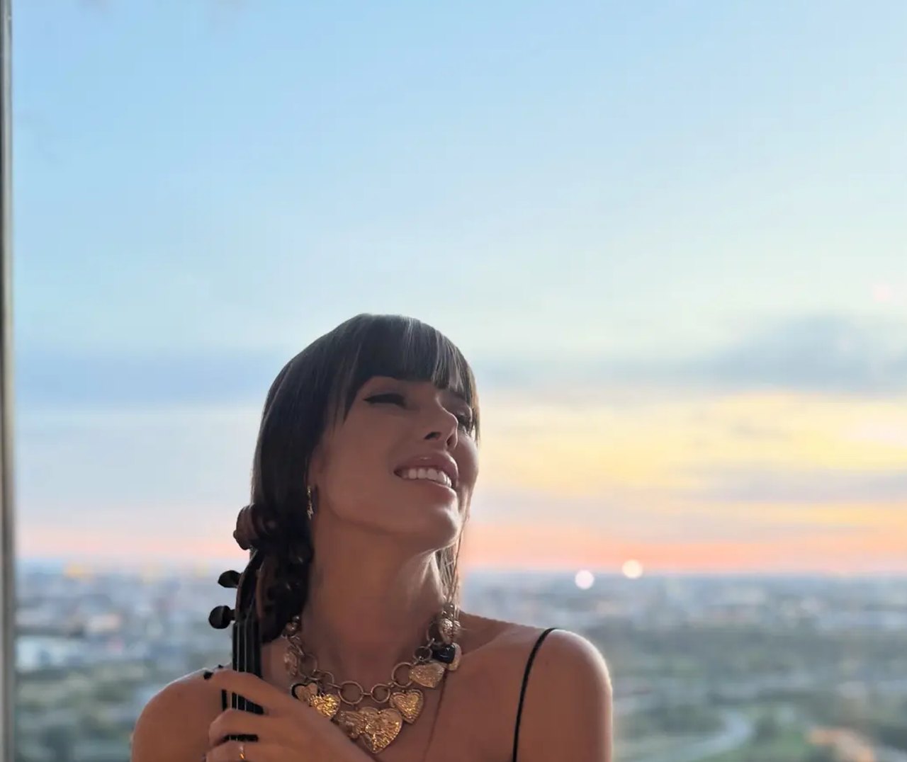 Astrid Torrente sonriendo con su violín acústico al atardecer frente a una vista panorámica