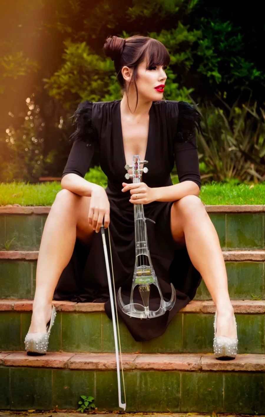 Astrid Torrente posando con su violín eléctrico sentada en una escalinata exterior