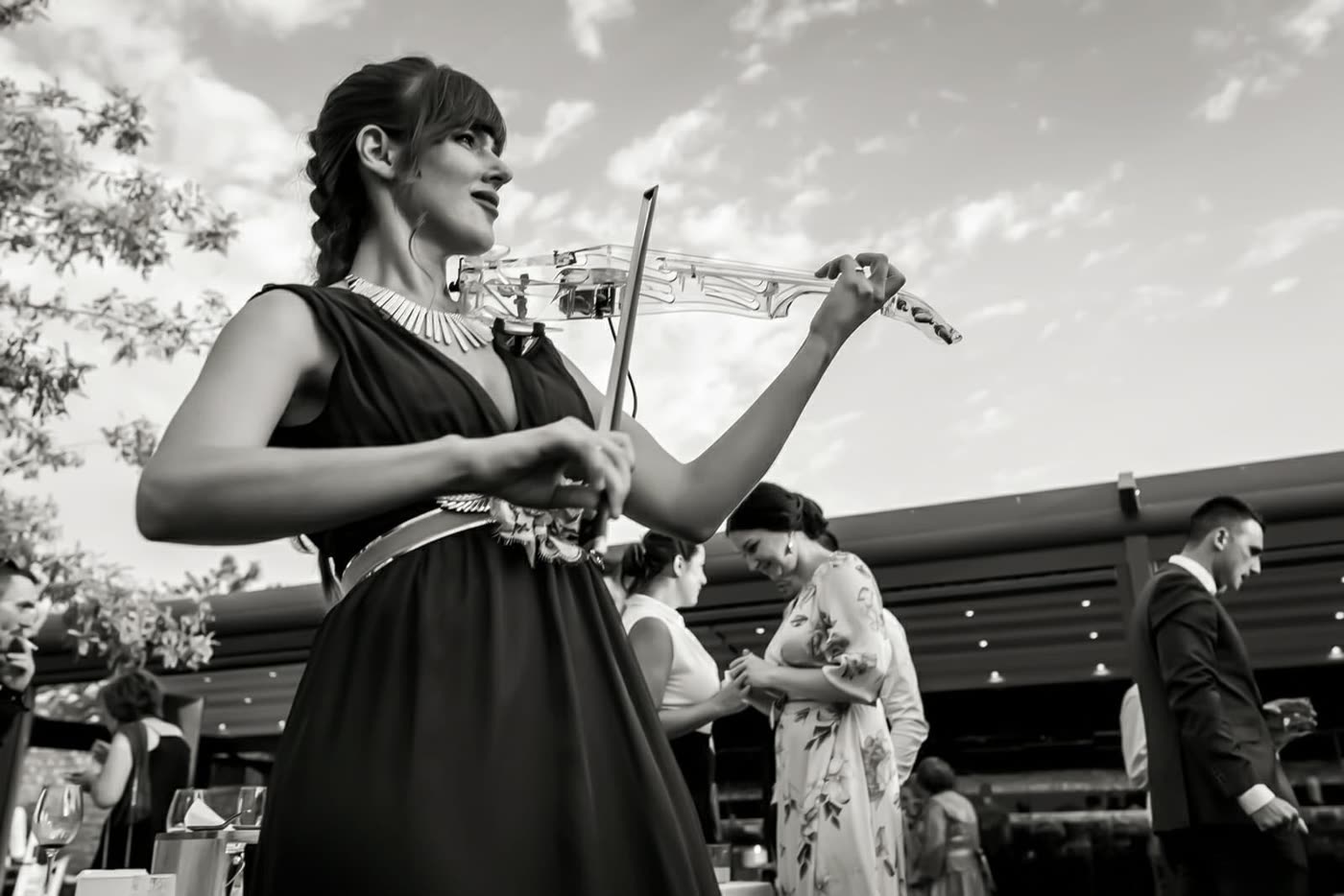 Astrid Torrente tocando el violín transparente entre los invitados de una boda, en blanco y negro
