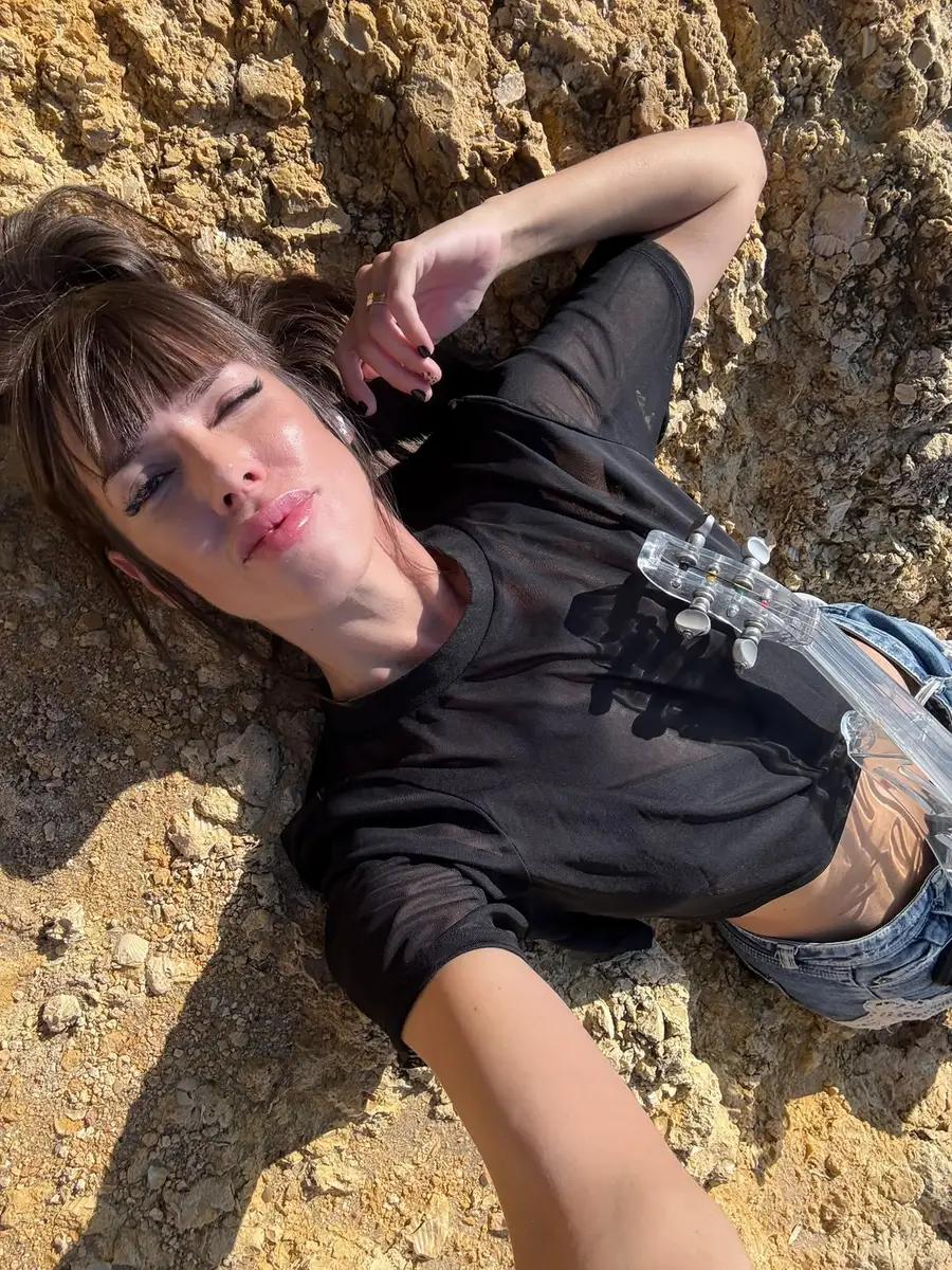 Astrid Torrente tumbada con su violín eléctrico en un entorno natural rocoso