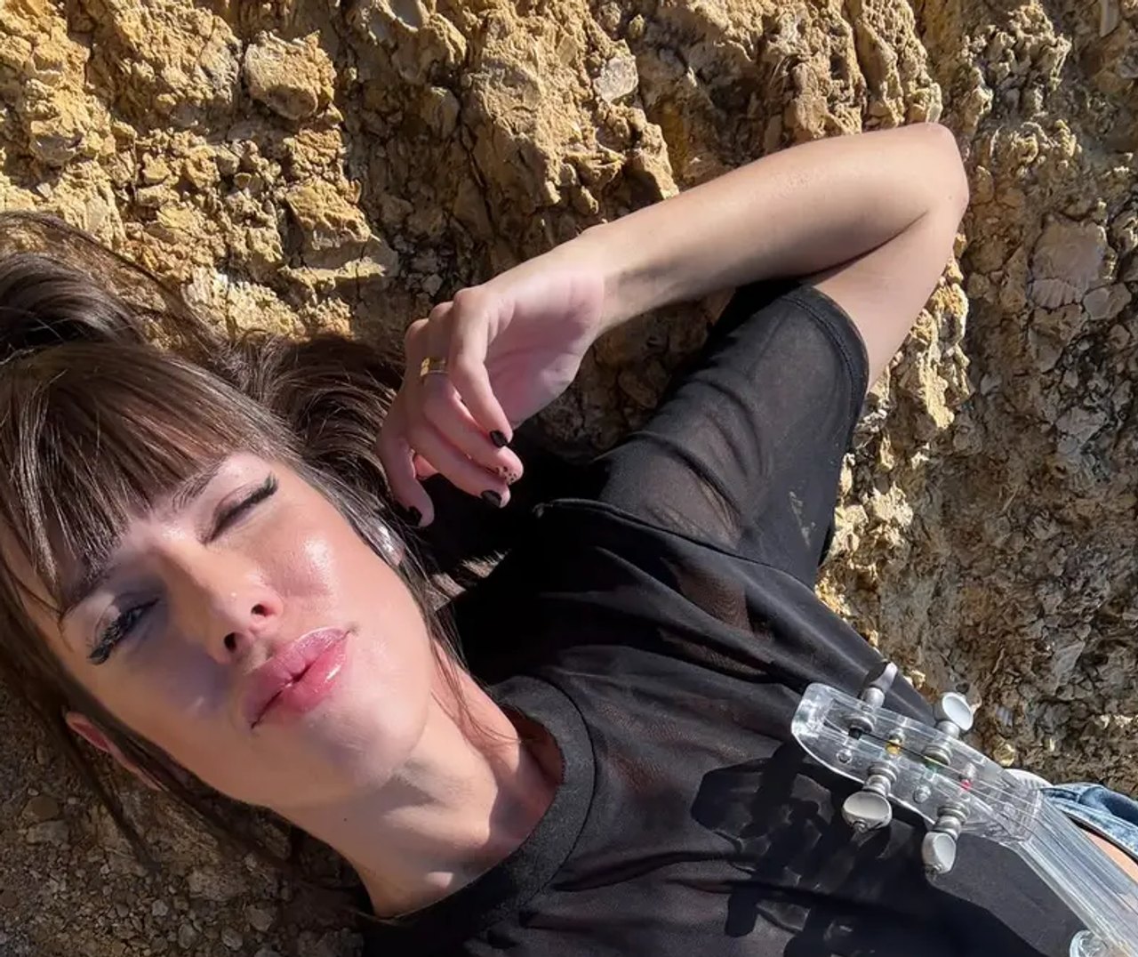 Astrid Torrente tumbada con su violín eléctrico en un entorno natural rocoso