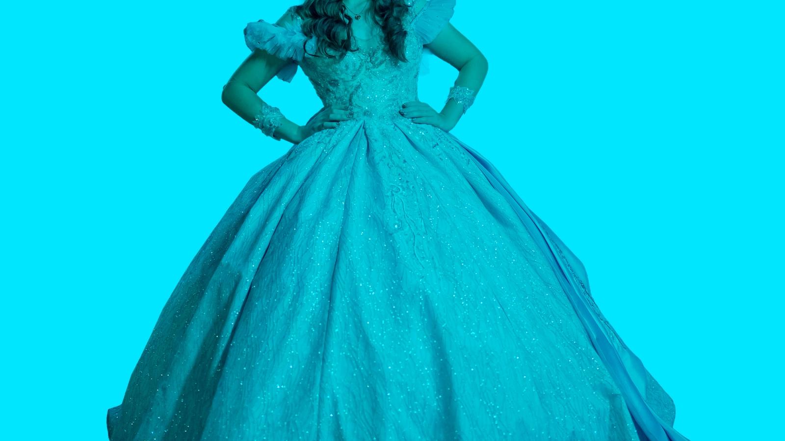 A person in a sparkly princess ball gown with hands on hips, against a teal background