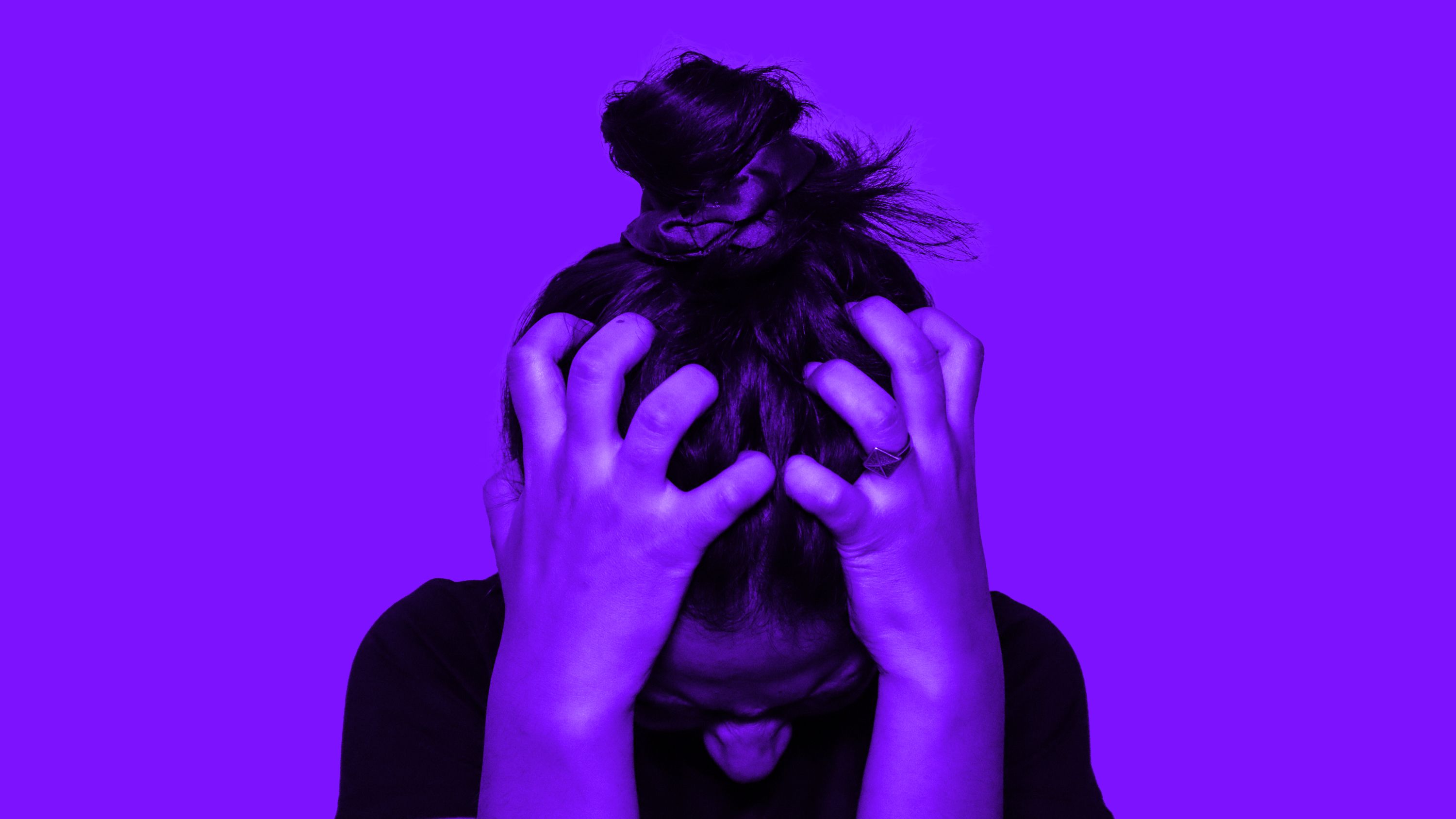 A person gripping their head in frustration against a purple background