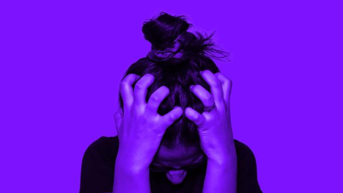 A person gripping their head in frustration against a purple background