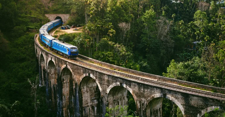 A blue train crossing the Nine Arches Bridge through the hills of Ella