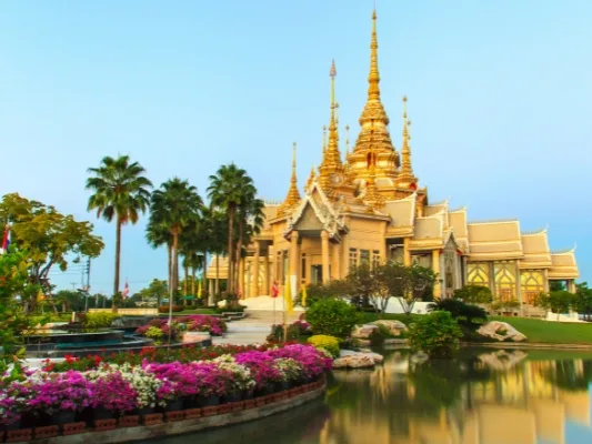 Golden Thai temple with ornate spires surrounded by palm trees and a reflecting pool